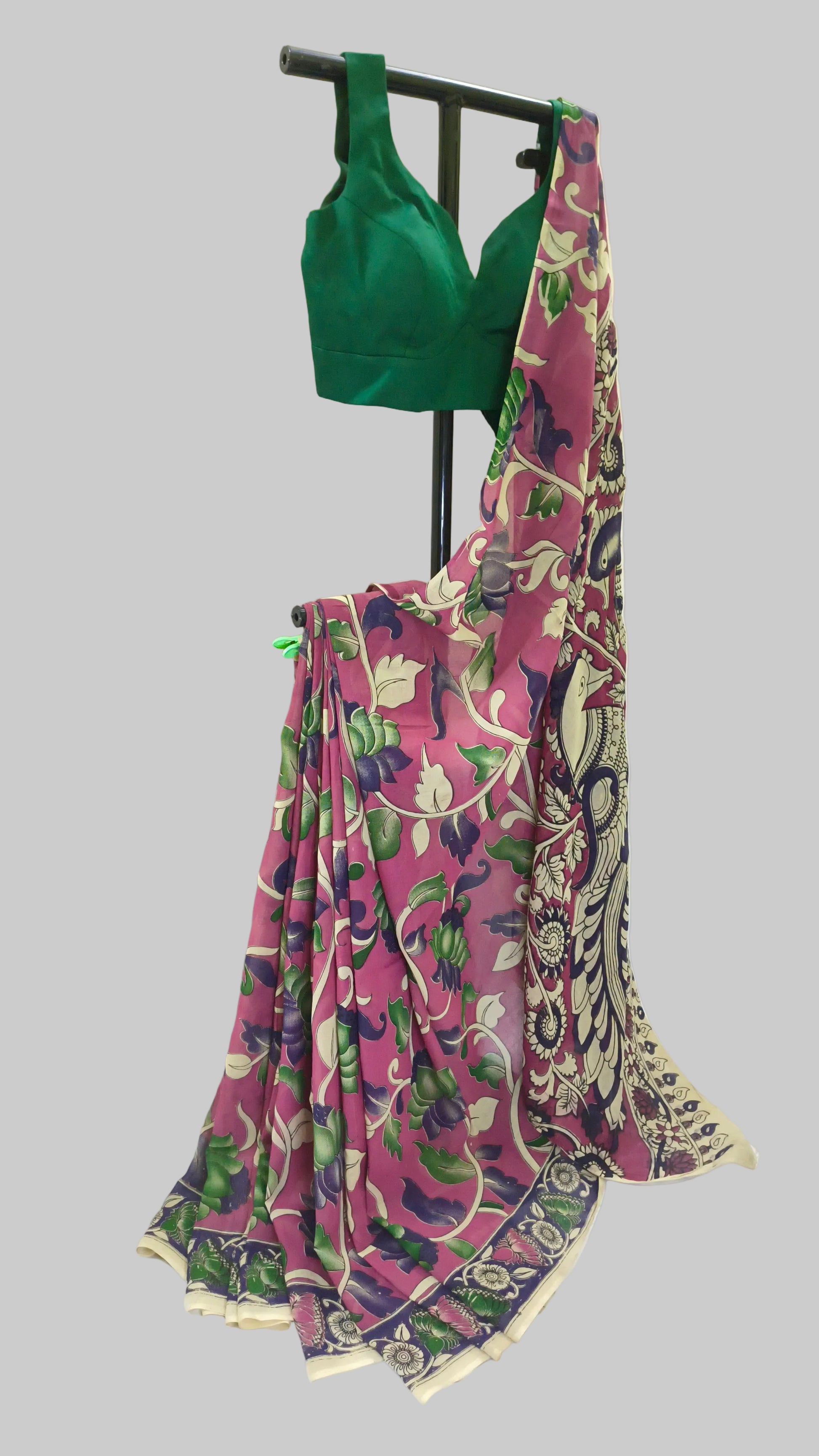 A pink floral printed saree with a green blouse displayed on a black clothing stand against a white backdrop.