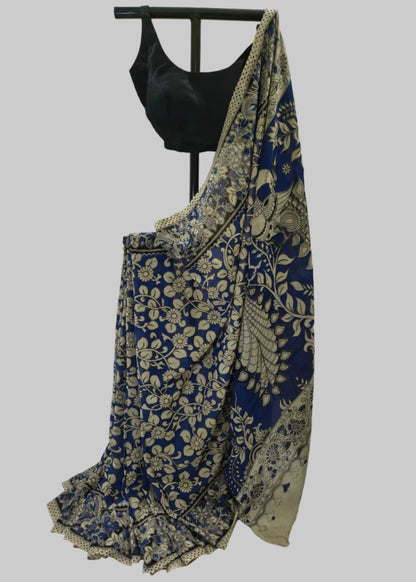 A blue and beige floral saree draped on a black dress form, paired with a black blouse, set against a draped white fabric backdrop.