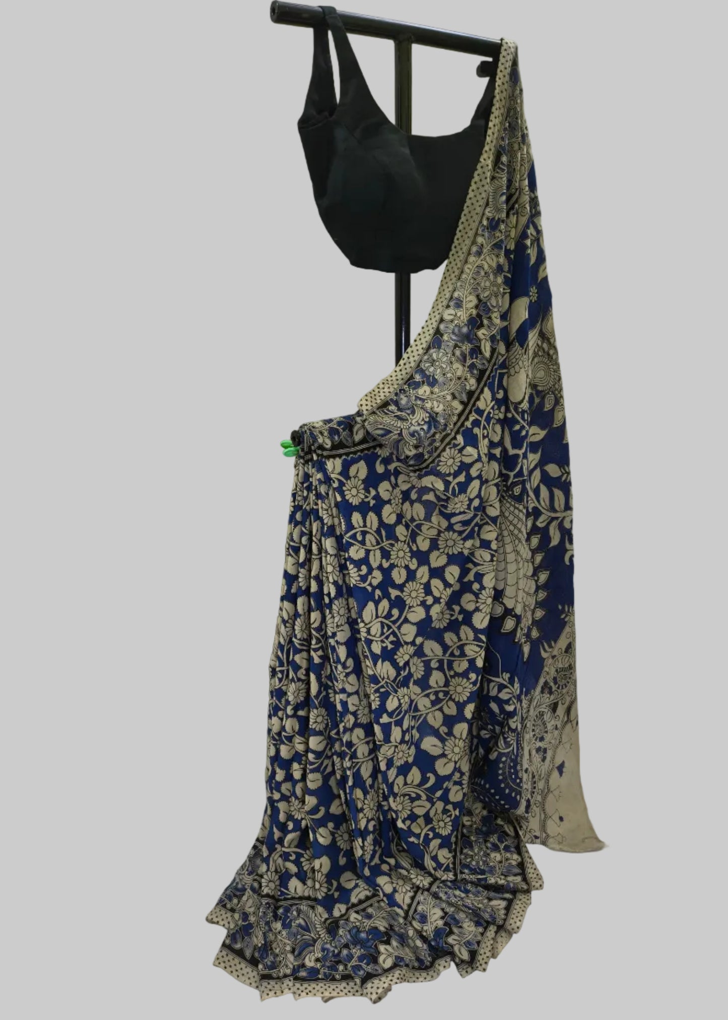 A blue and beige floral printed saree draped on a black dress form, paired with a black blouse, set against a white fabric backdrop.