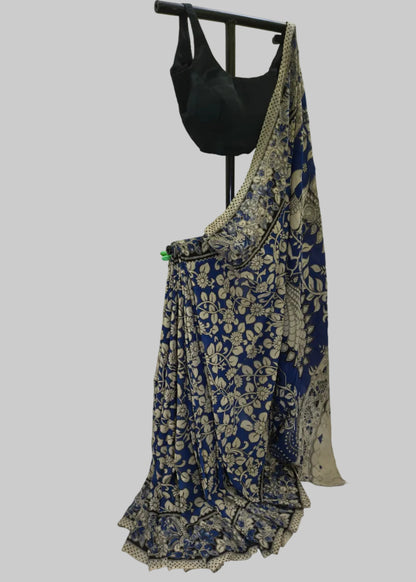 A blue and beige floral printed saree draped on a black dress form, paired with a black blouse, set against a white fabric backdrop.