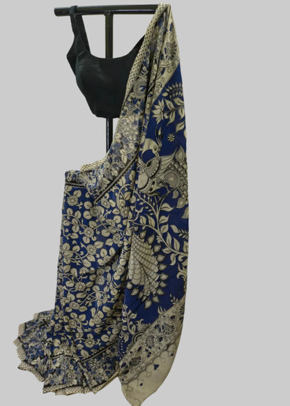 A blue and beige floral saree draped on a black dress form, paired with a black sleeveless blouse, set against a draped cream fabric backdrop.