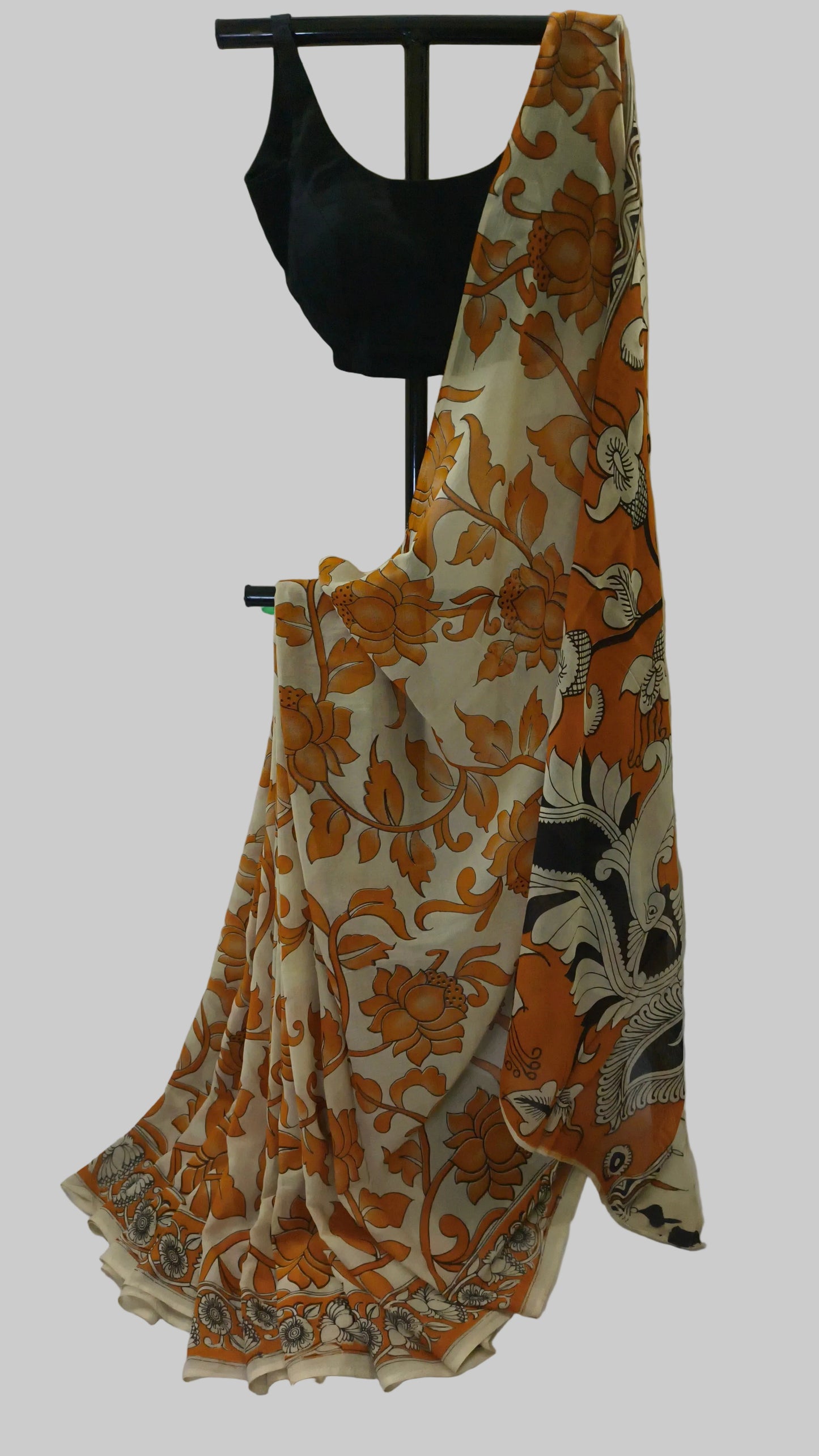 A beige saree with a bold orange floral and vine pattern, draped on a black dress form, accompanied by a solid black blouse.
