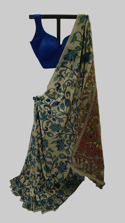 A beige saree with blue floral patterns and a red patterned border, paired with a royal blue blouse, displayed on a black hanger against a white draped backdrop.