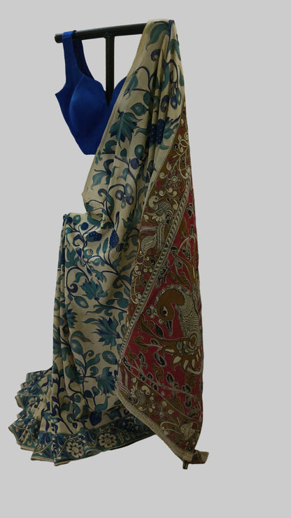 A draped saree with a blue floral pattern on a beige base and a red patterned pallu, displayed on a black hanger with a royal blue blouse against a white draped backdrop.