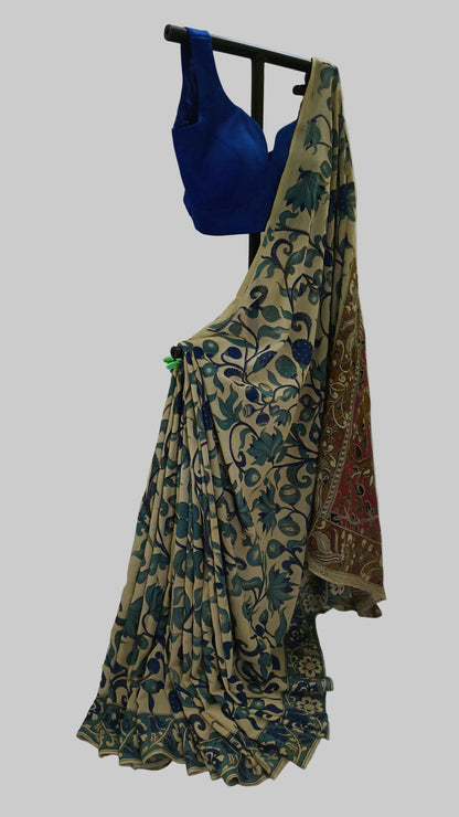 A beige and blue printed saree with a blue blouse displayed on a black dress form against a white fabric backdrop.