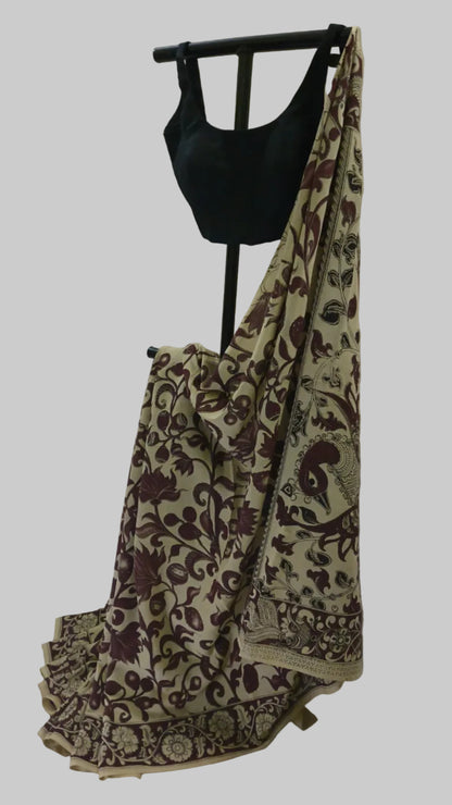 A beige and brown floral printed saree draped on a black dress form, paired with a black sleeveless blouse, set against a draped white fabric backdrop.