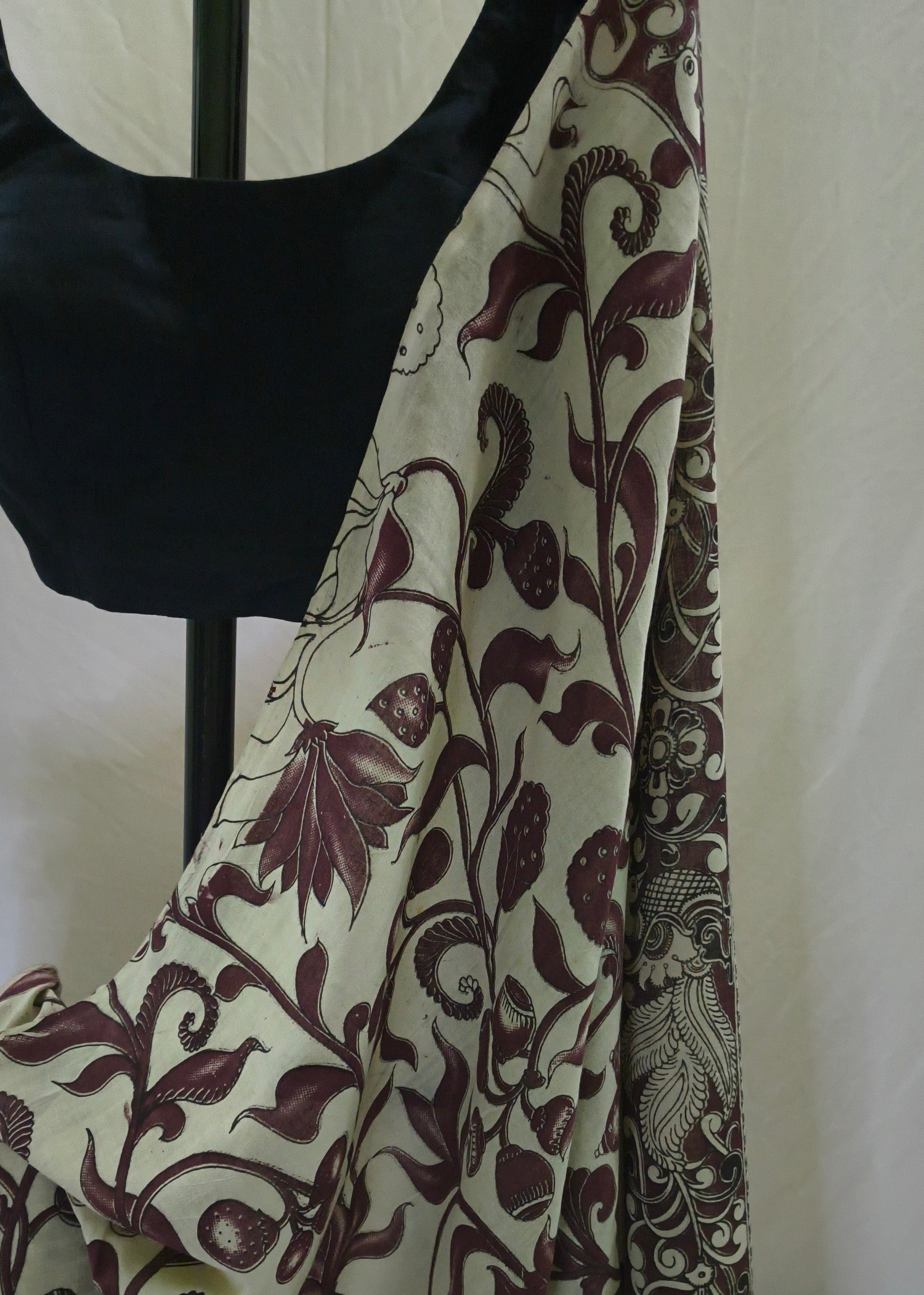 A draped saree or fabric panel with a cream base and dark burgundy floral vine pattern, displayed on a black dress form against a light neutral backdrop.