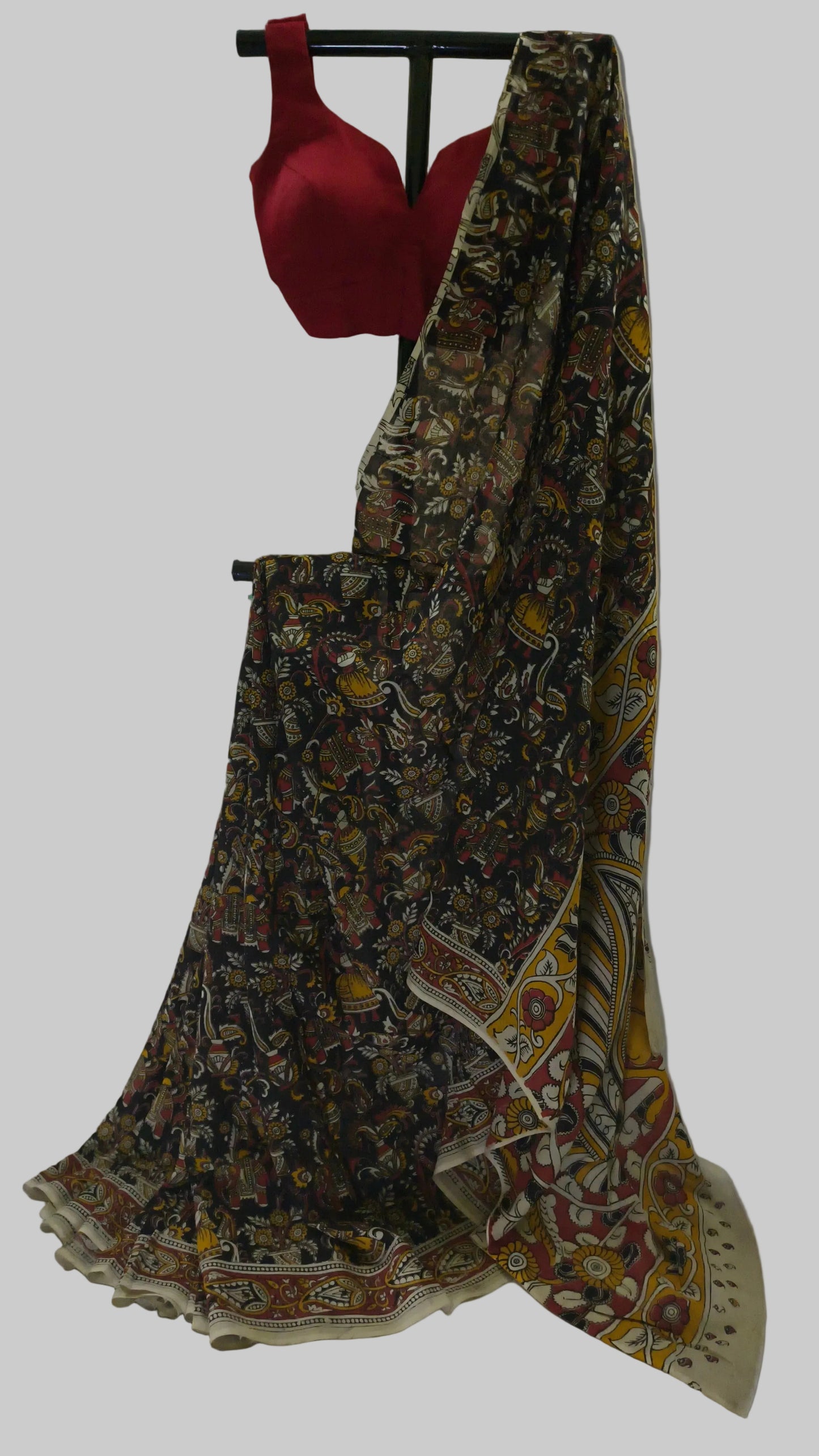 A traditional Indian saree with a black base and a multicolor floral print, paired with a solid red blouse, displayed on a stand against a white fabric backdrop.