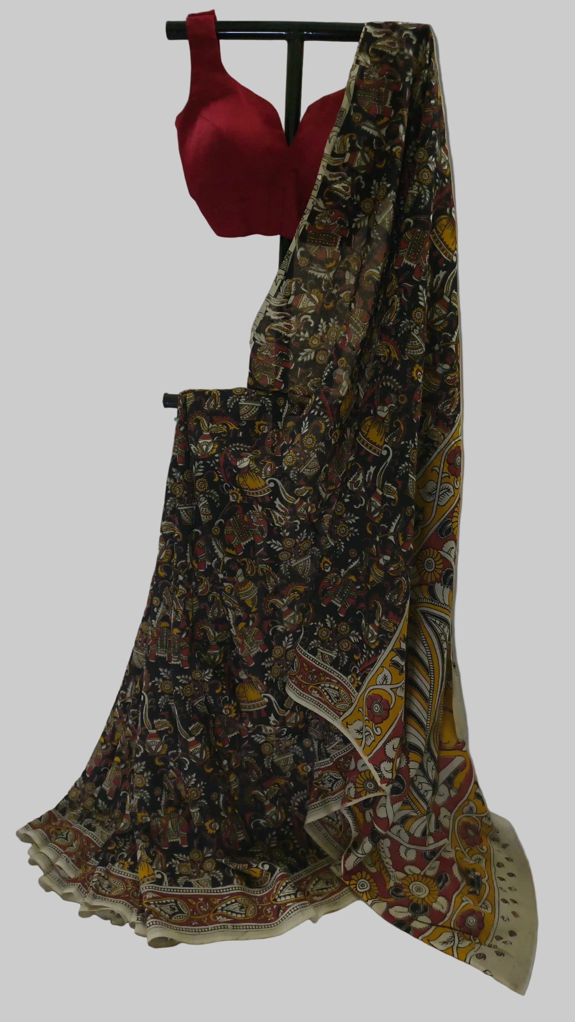 A traditional Indian saree with a black base and a multicolor floral print, paired with a solid red blouse, displayed on a stand against a white fabric backdrop.