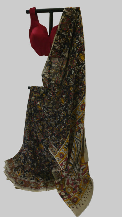 A traditional Indian saree with a dark brown and beige floral print, draped on a black clothing hanger next to a red blouse, set against a draped white fabric backdrop.