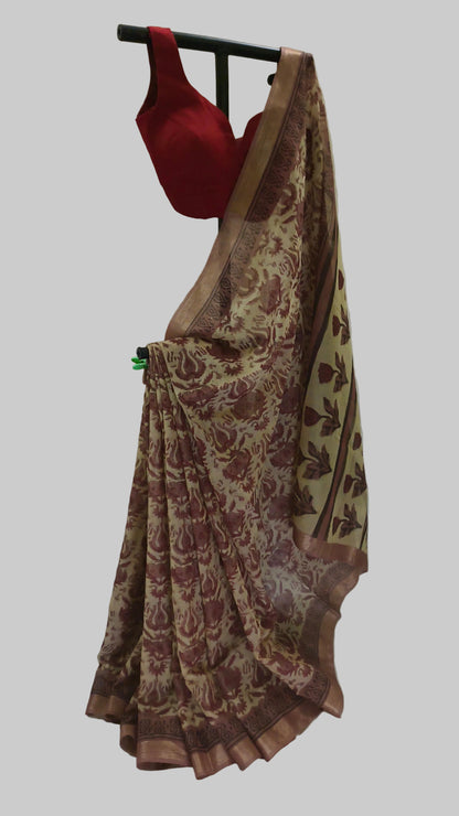 A beige and brown floral printed saree draped on a black hanger, paired with a solid red blouse, set against a draped white fabric backdrop.