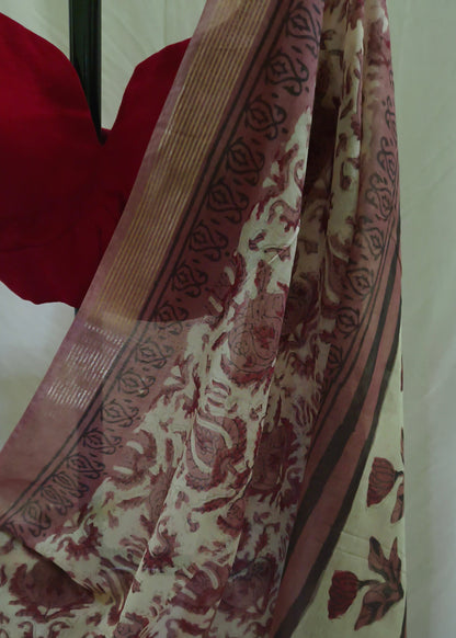 A close-up of a patterned saree or fabric draped over a mannequin, featuring a cream base with reddish-brown floral motifs and a matching red blouse visible at the top left.