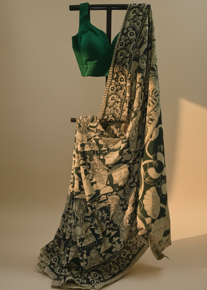 A black and beige patterned saree draped elegantly on a stand, paired with a dark green sleeveless blouse, displayed against a warm beige background.