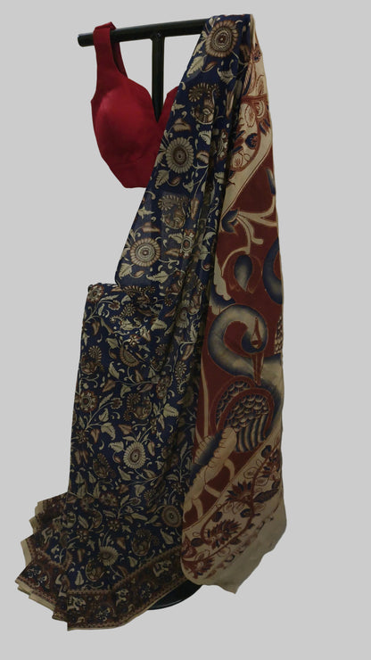 A traditional Indian saree draped on a black clothing stand, featuring a navy blue floral patterned body, a beige border with red and blue paisley motifs, and a solid red blouse attached at the top.