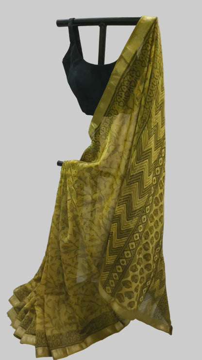 A yellow-green patterned saree draped over a black dress form, paired with a black blouse, set against a white fabric backdrop.