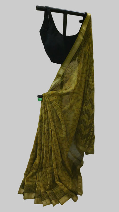 A yellow-gold patterned saree with a black blouse displayed on a black hanger against a white fabric backdrop.