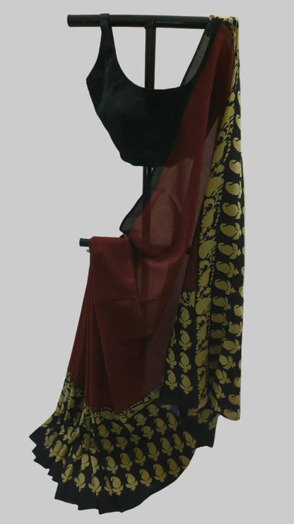 A black and maroon saree with gold floral patterns, displayed on a black clothing stand with a black blouse against a draped cream fabric background.