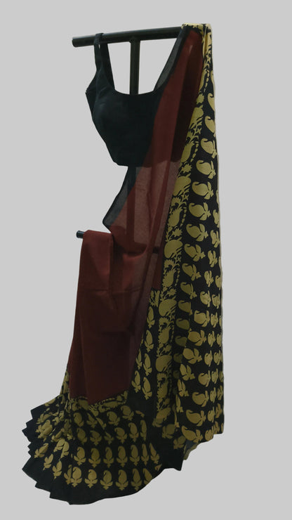 A black and maroon saree with a gold floral pattern on the pallu, displayed on a black clothing rack against a draped off-white fabric backdrop.