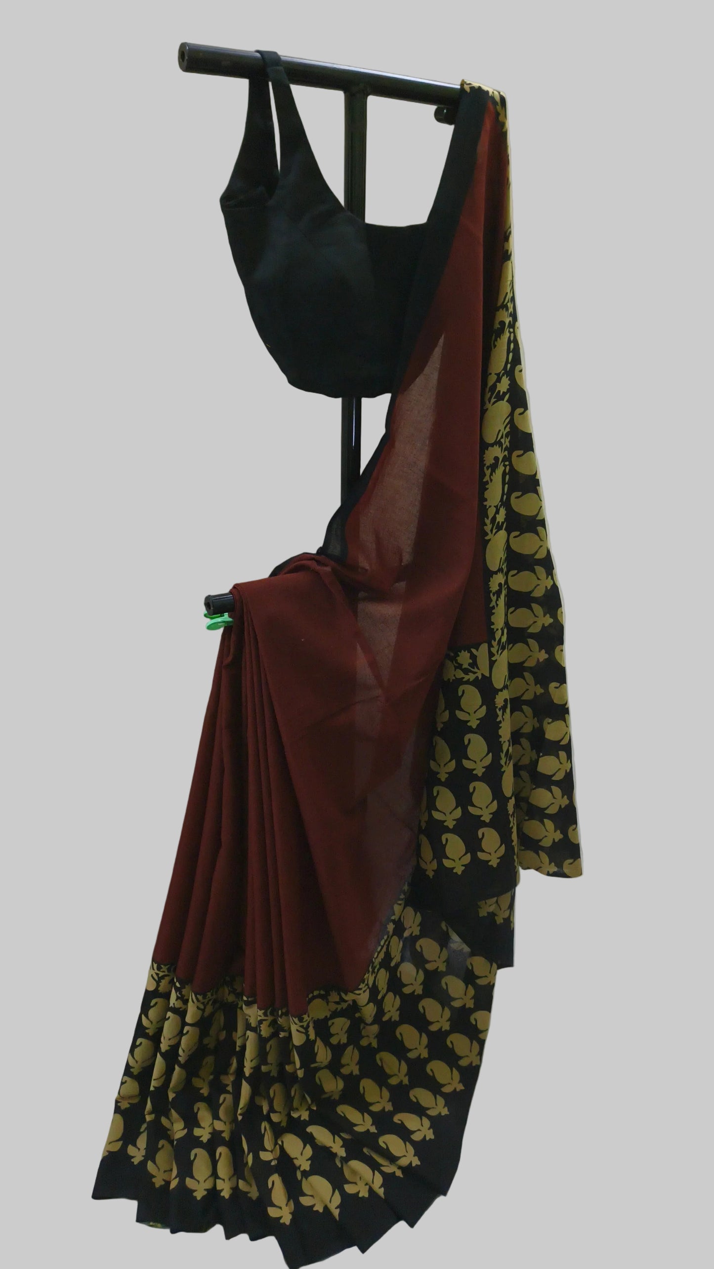 A black and maroon saree with gold floral patterns draped on a black clothing stand against a white fabric backdrop.