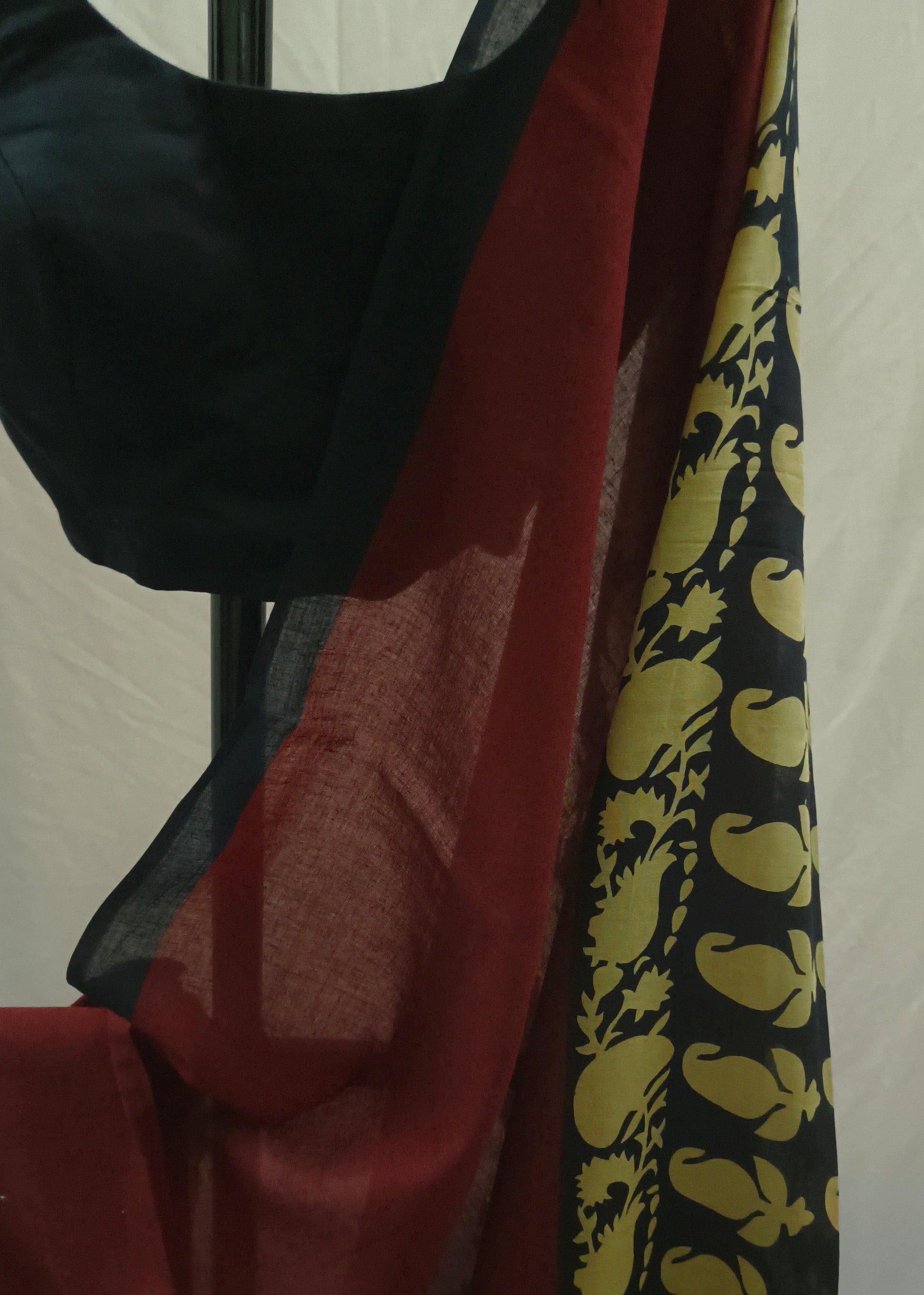 A draped black and red saree or fabric set with a black blouse piece, shown against a plain light background. The fabric features a deep red body with a black border decorated with a yellow paisley pattern.