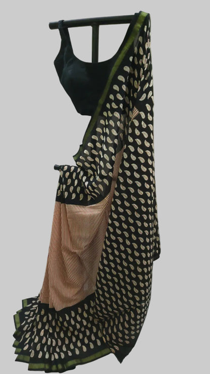 A black and beige patterned saree with a peach-beige striped pallu and a black sleeveless blouse, displayed on a hanger against a white fabric backdrop.