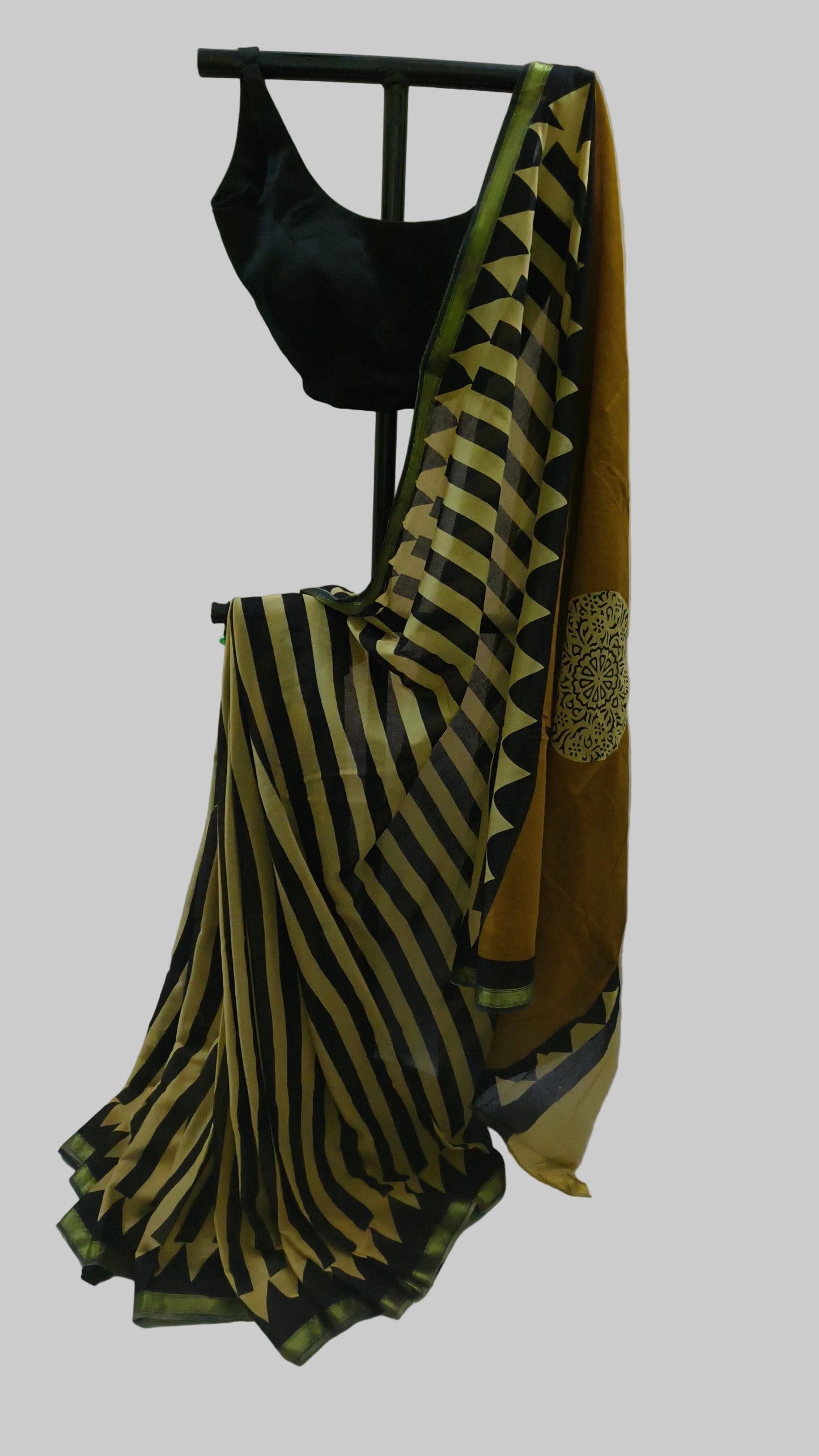 A black and mustard yellow striped saree draped on a black clothing stand, paired with a black sleeveless blouse, set against a white fabric backdrop.
