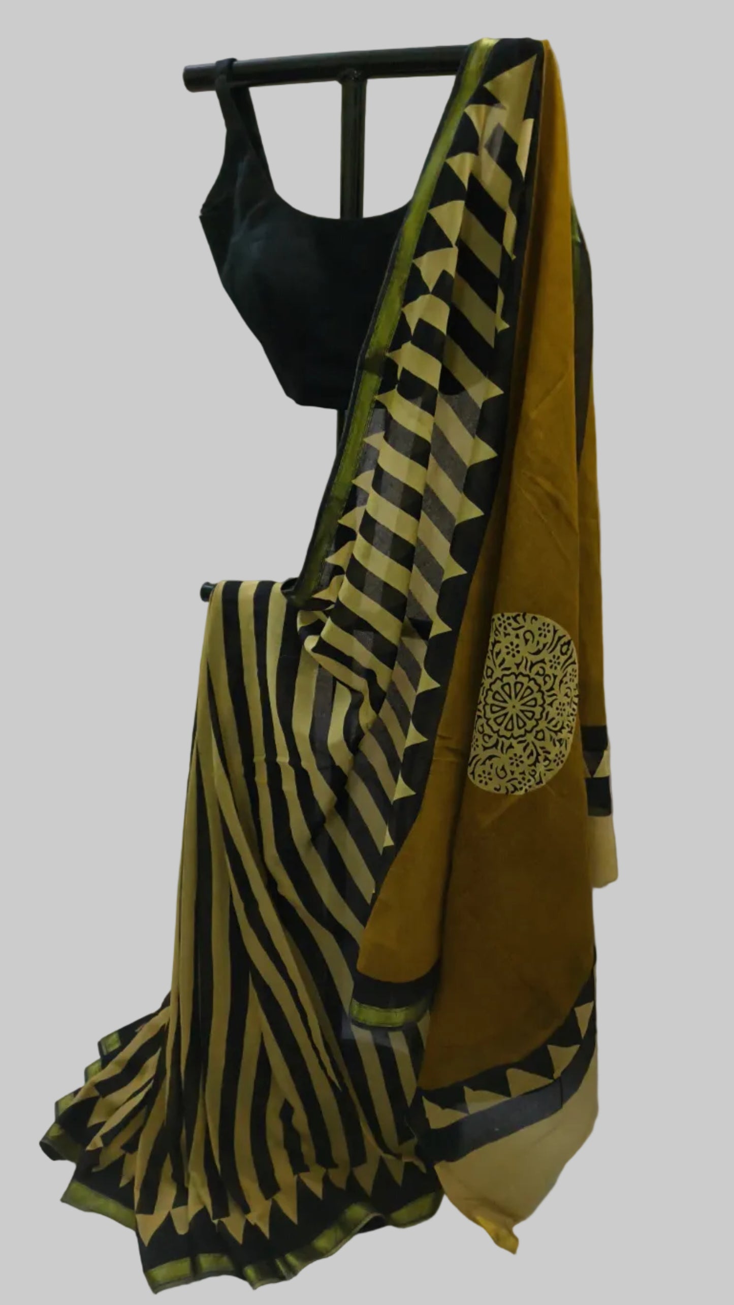 A black and mustard yellow striped saree draped on a black hanger with a black sleeveless blouse, set against a white fabric backdrop.