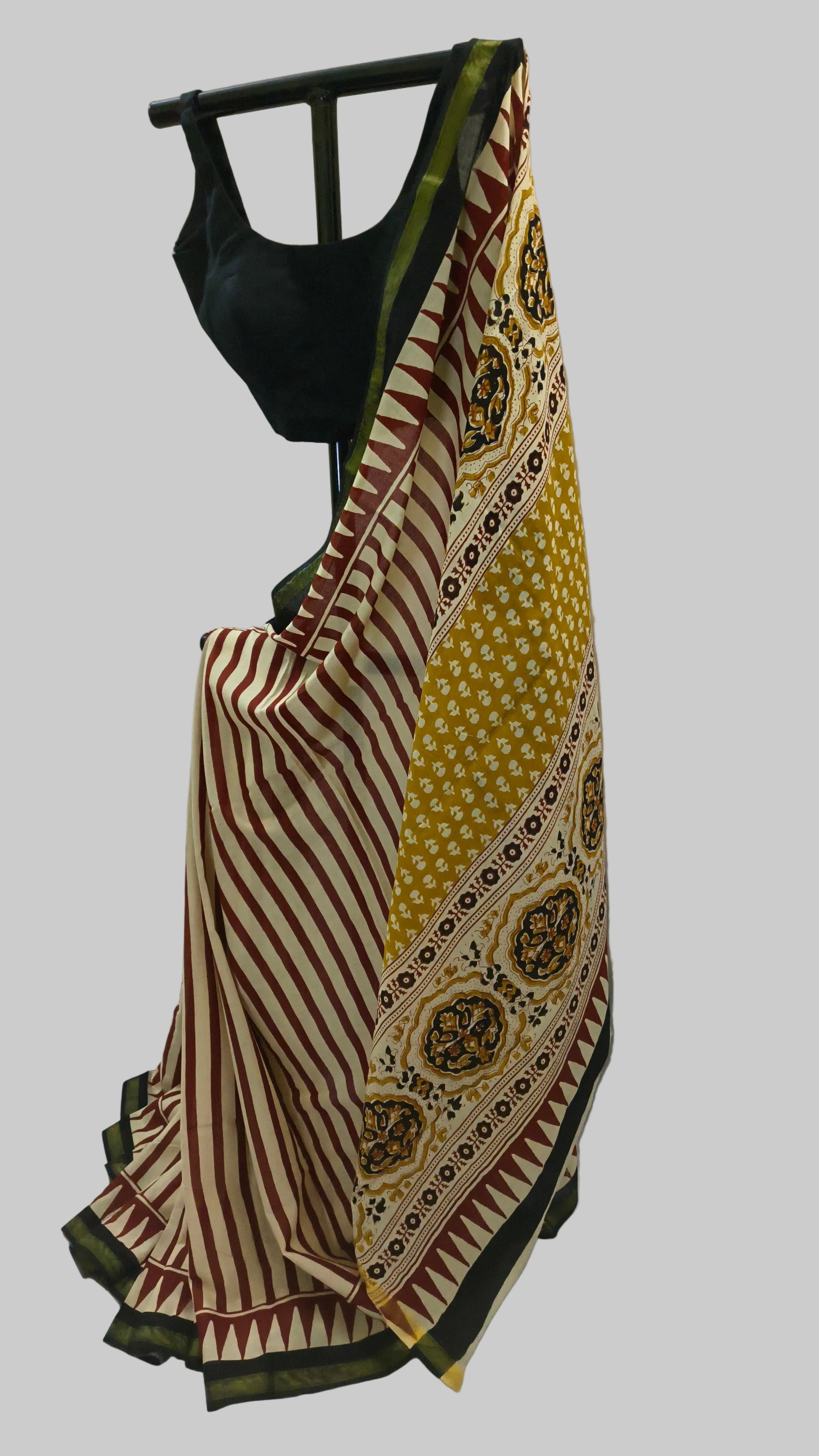 A patterned Indian saree draped on a black hanger with a black blouse, set against a draped white fabric backdrop.