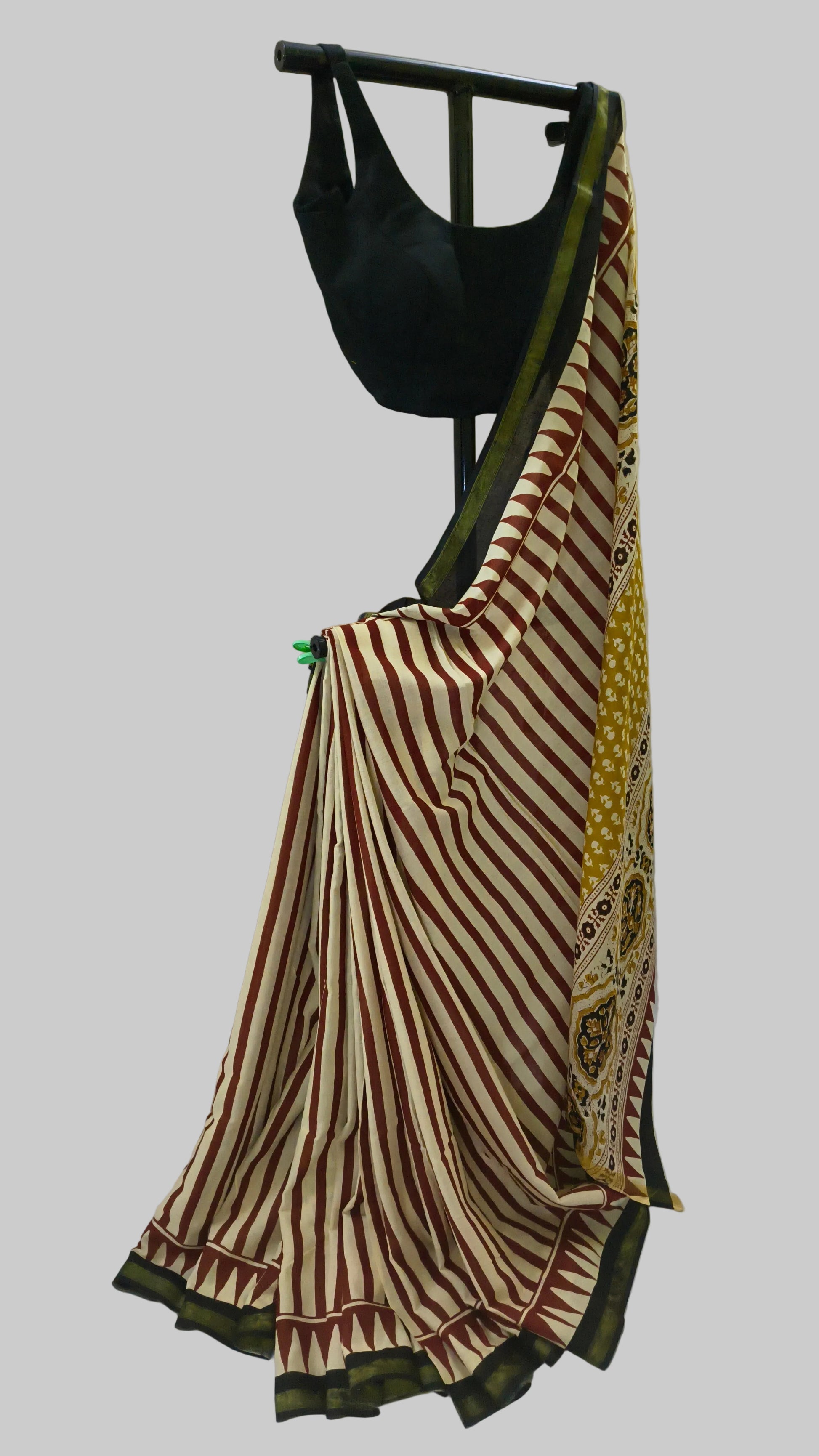 A striped cotton saree draped on a black clothing hanger with a black blouse, set against a white fabric backdrop.