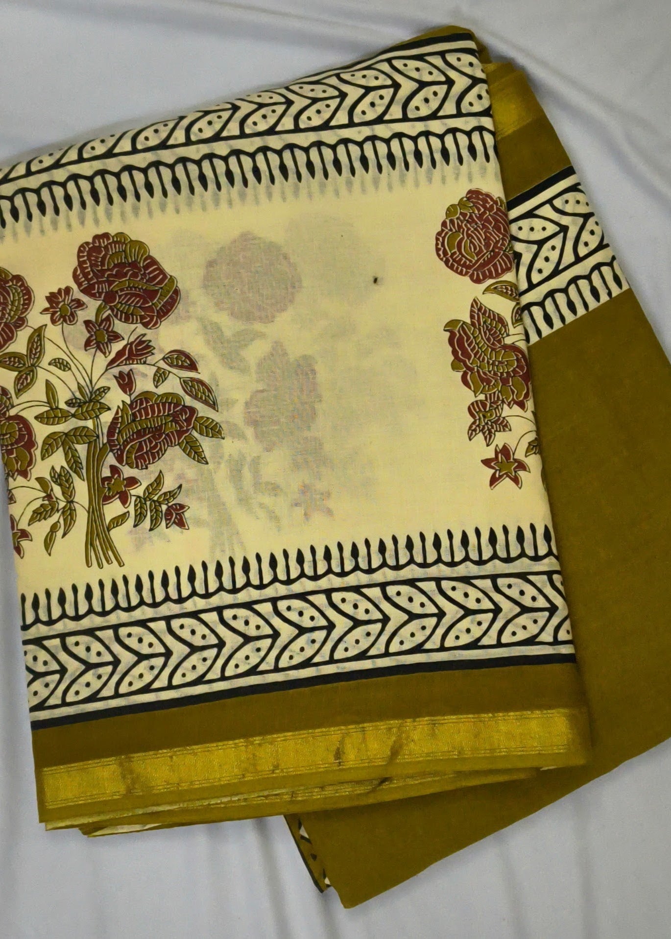 A folded piece of traditional Indian saree fabric, featuring a cream-colored body with a printed floral pattern and borders, paired with a solid mustard yellow border.