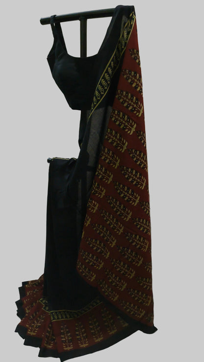 A black sleeveless blouse with a matching black skirt or drape, displayed on a black hanger against a white fabric backdrop. The fabric features a prominent red border with gold and black traditional patterns.