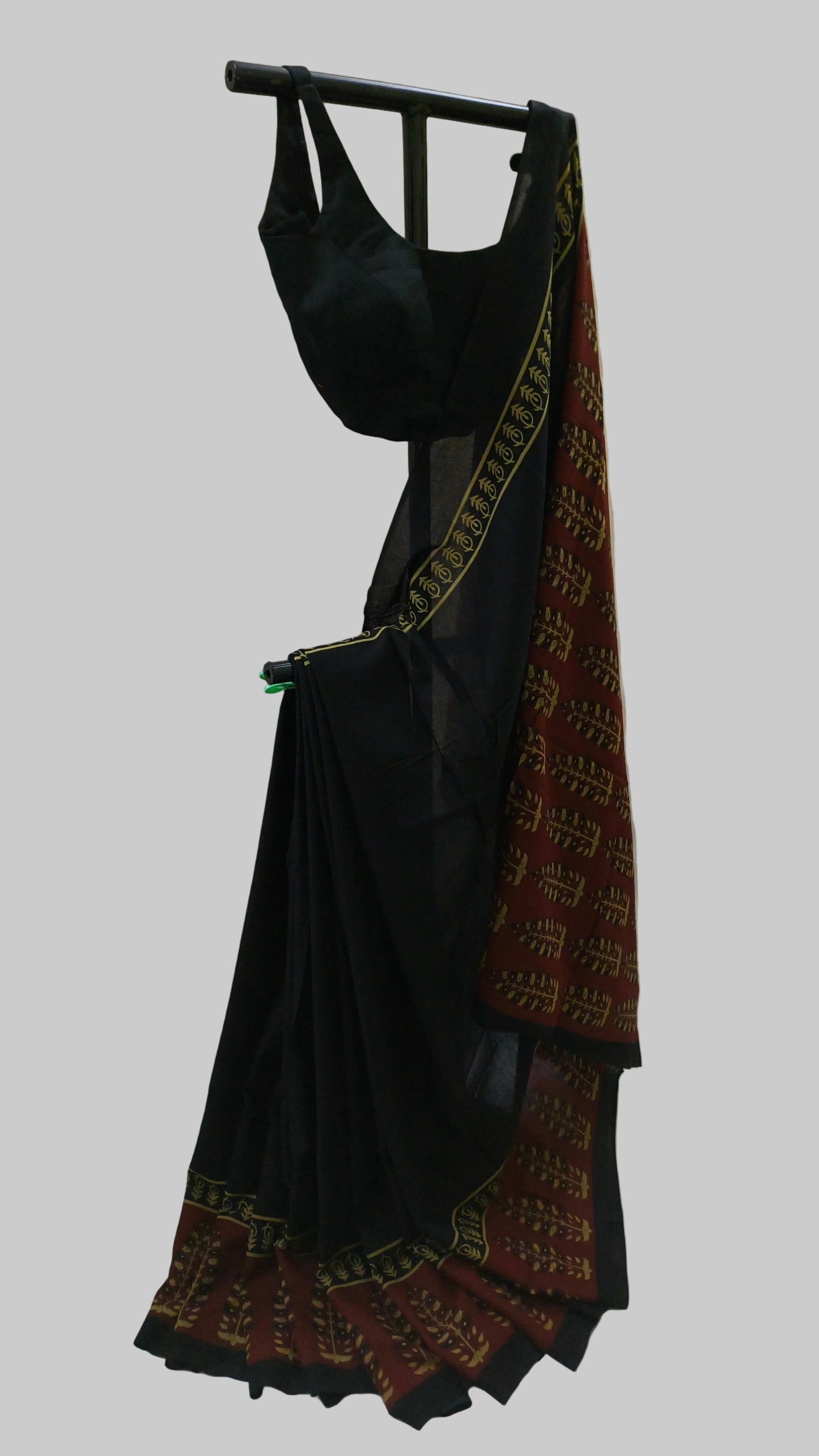 A black saree with a red and gold patterned border, draped on a black hanger against a white fabric backdrop.