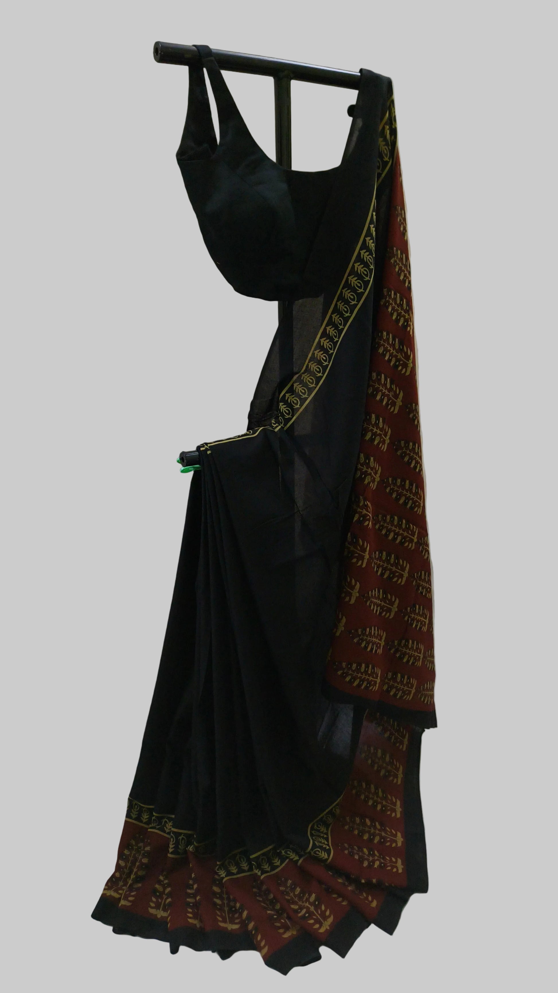 A black saree with a red and gold patterned border, draped on a black hanger against a white fabric backdrop.