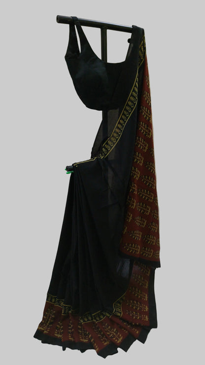 A black saree with a red and gold patterned border, draped on a black hanger against a white fabric backdrop.