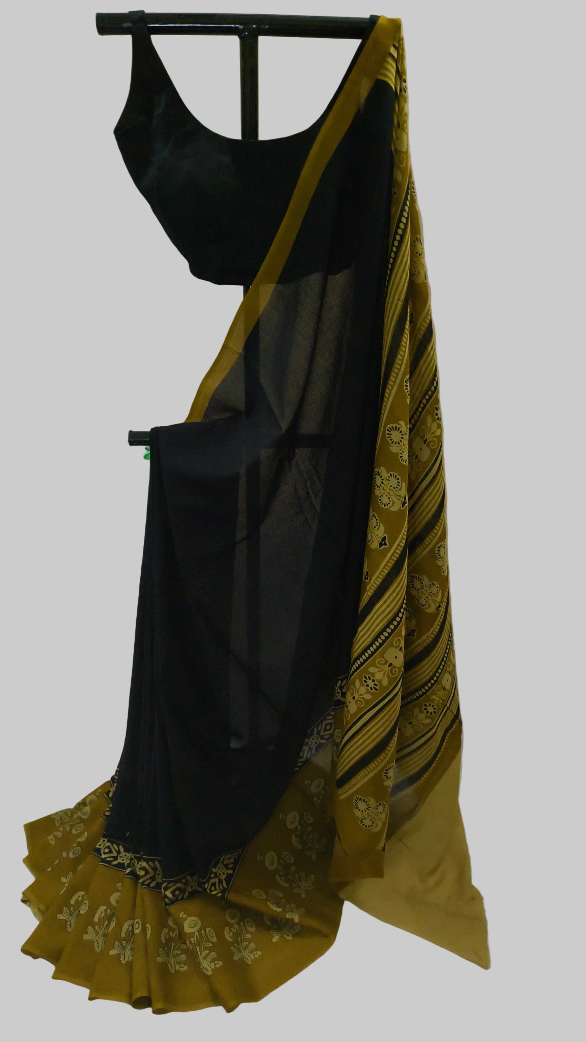 A black georgette saree with a mustard yellow border and gold floral patterns, displayed on a black hanger with a matching black blouse.