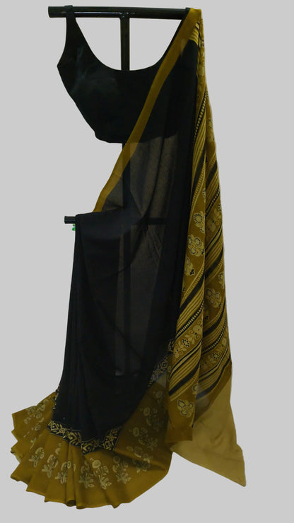 A black georgette saree with a mustard yellow border and gold floral patterns, displayed on a black hanger with a matching black blouse.