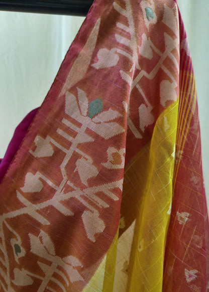 A close-up of a draped patterned fabric, likely a saree or scarf, featuring a rust-red base with white floral motifs and a prominent yellow border.