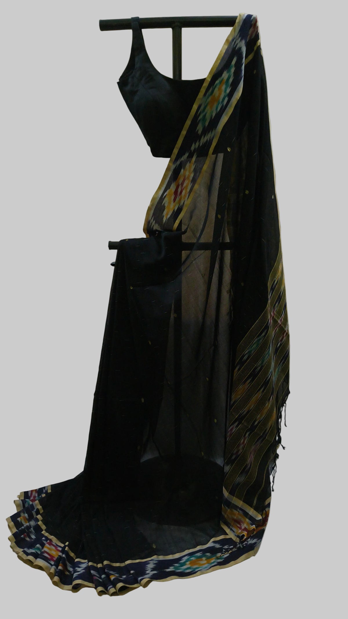 A black georgette saree with a matching black blouse and a black dupatta draped over a black hanger, featuring a colorful ikat border pattern in blue, yellow, and green.