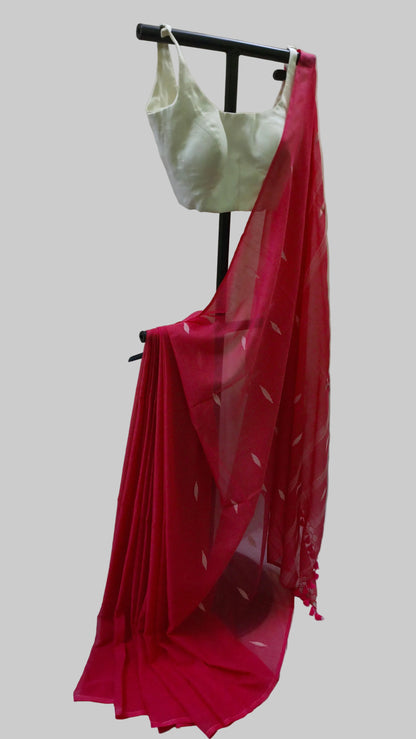 A bright pinkish-red saree with a white sleeveless blouse displayed on a black clothing stand against a beige curtain backdrop.