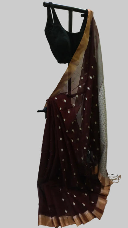 A dark maroon sheer saree with small metallic gold motifs and a wide gold border, draped over a black blouse on a stand against a white fabric backdrop.