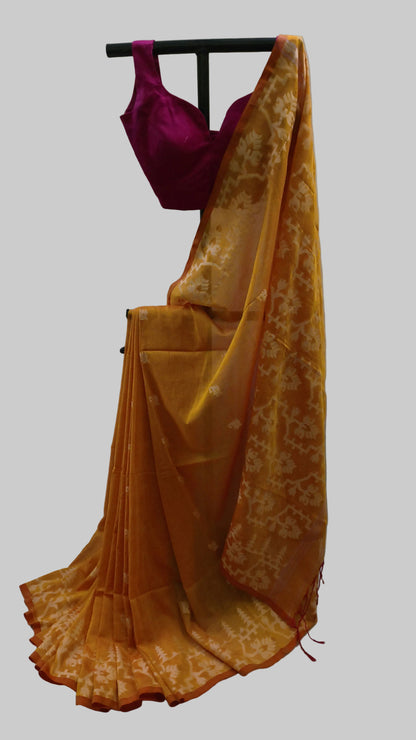 An orange saree with a white floral pattern and a magenta purple blouse, displayed on a black clothing stand against a white curtain backdrop.