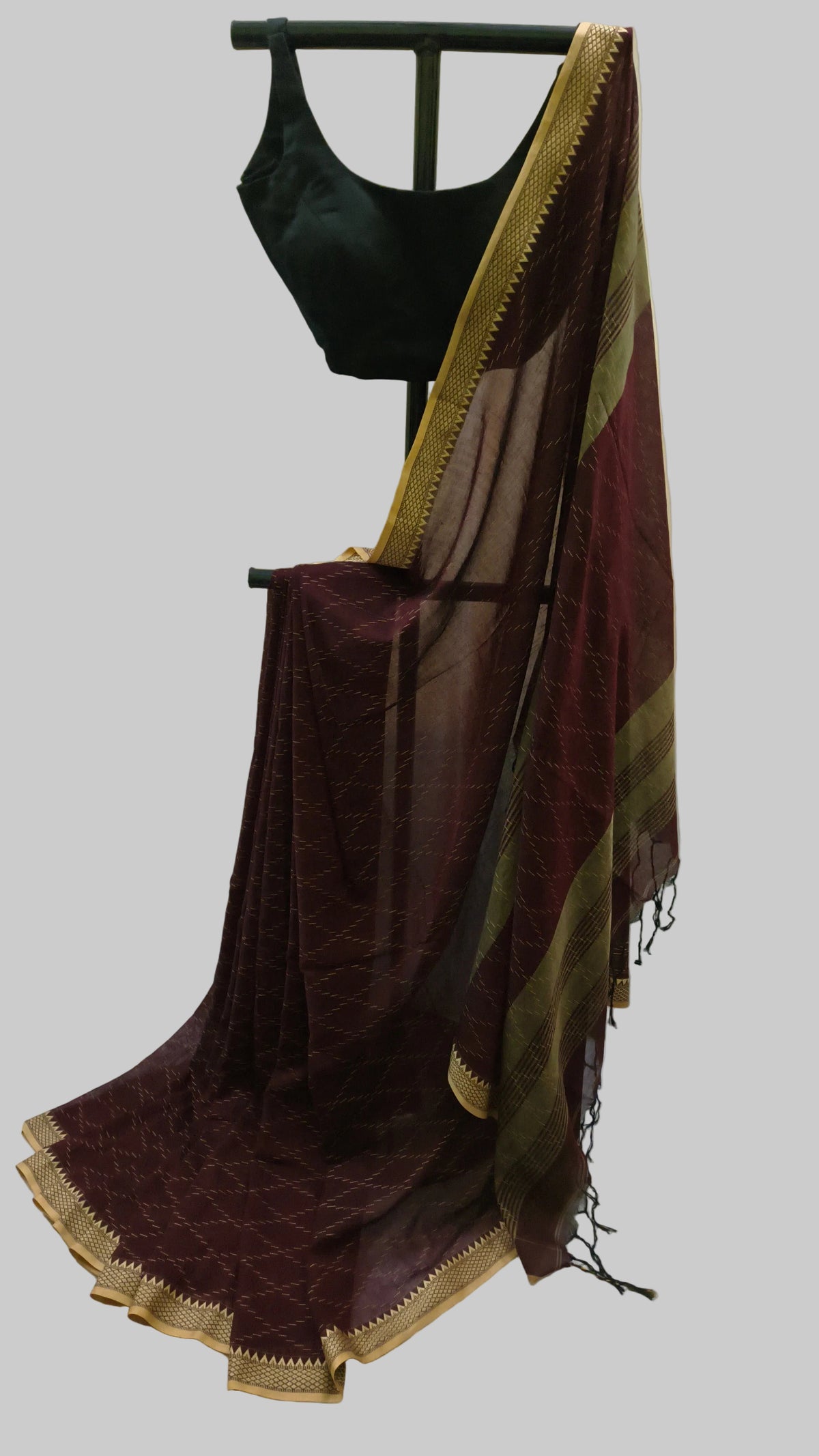 A dark maroon sheer saree with gold zari borders and a black sleeveless blouse displayed on a black hanger against a cream-colored backdrop.