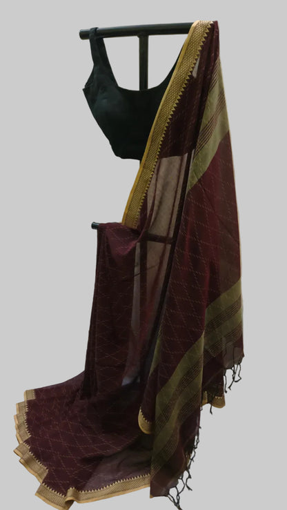 A dark maroon saree with gold borders and a black blouse draped on a black clothing stand against a cream-colored curtain backdrop.