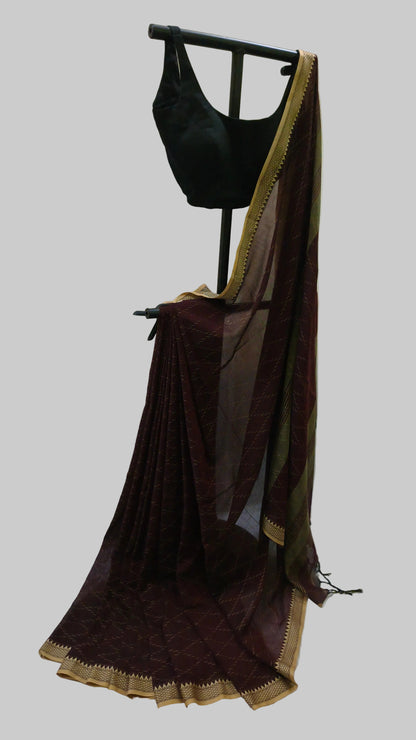 A dark maroon saree with a gold border and a black blouse displayed on a black clothing stand against a draped cream fabric backdrop.