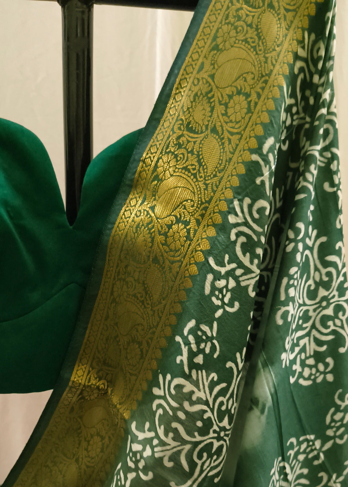 A close-up of a green saree with a wide gold zari border and white floral motifs, paired with a matching green blouse.