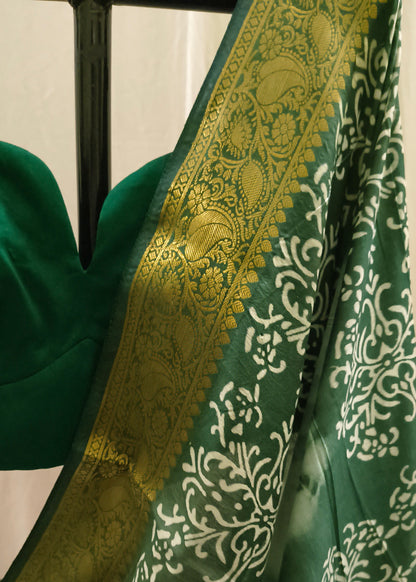 A close-up of a green saree with a wide gold zari border and white floral motifs, paired with a matching green blouse.