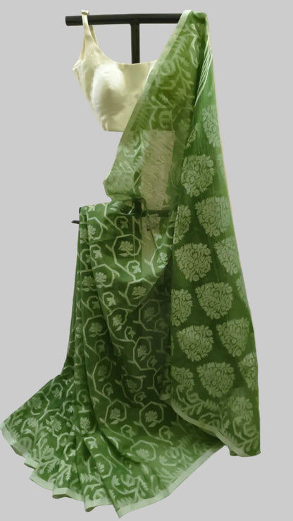 A green saree with a light green floral and vine pattern, draped on a black hanger with a light green blouse, set against a neutral beige curtain background.