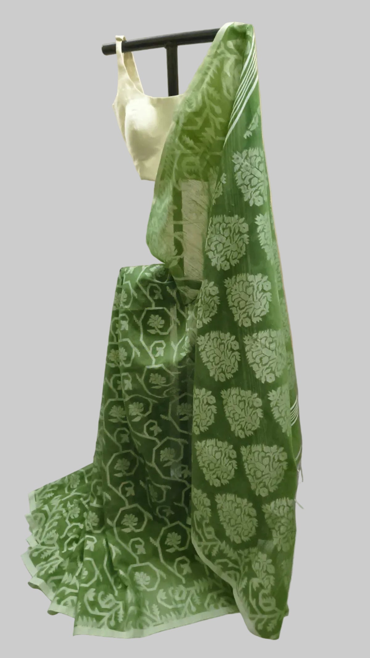 A green saree with white floral block prints draped over a black hanger stand, paired with a white sleeveless blouse, set against a cream-colored fabric backdrop.