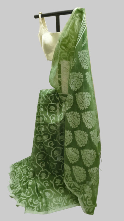 A green saree with white floral block prints draped over a black hanger stand, paired with a white sleeveless blouse, set against a cream-colored fabric backdrop.