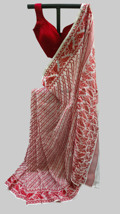 A red and white patterned saree draped on a black hanger with a matching red blouse, set against a neutral cream-colored backdrop.